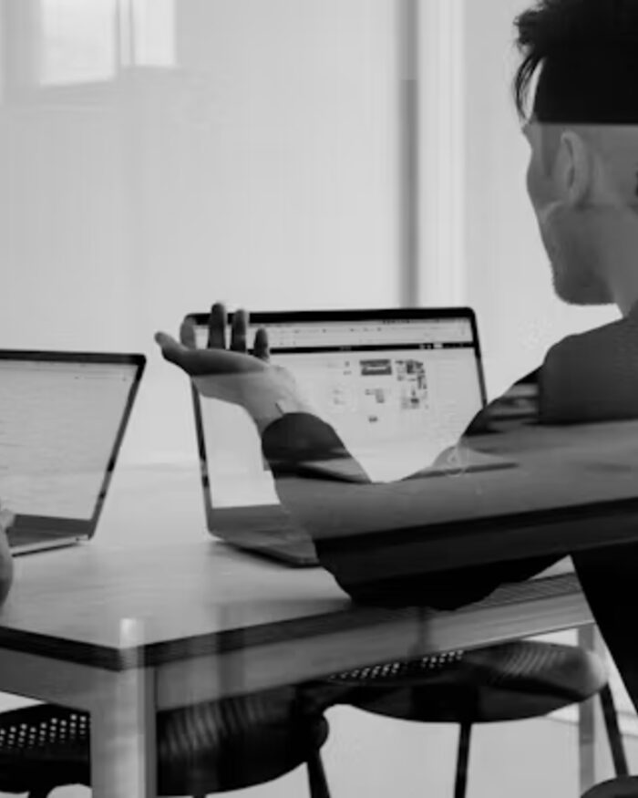 Two Meridian consultants working side by side at a laptop in a bright, quiet office, in black and white